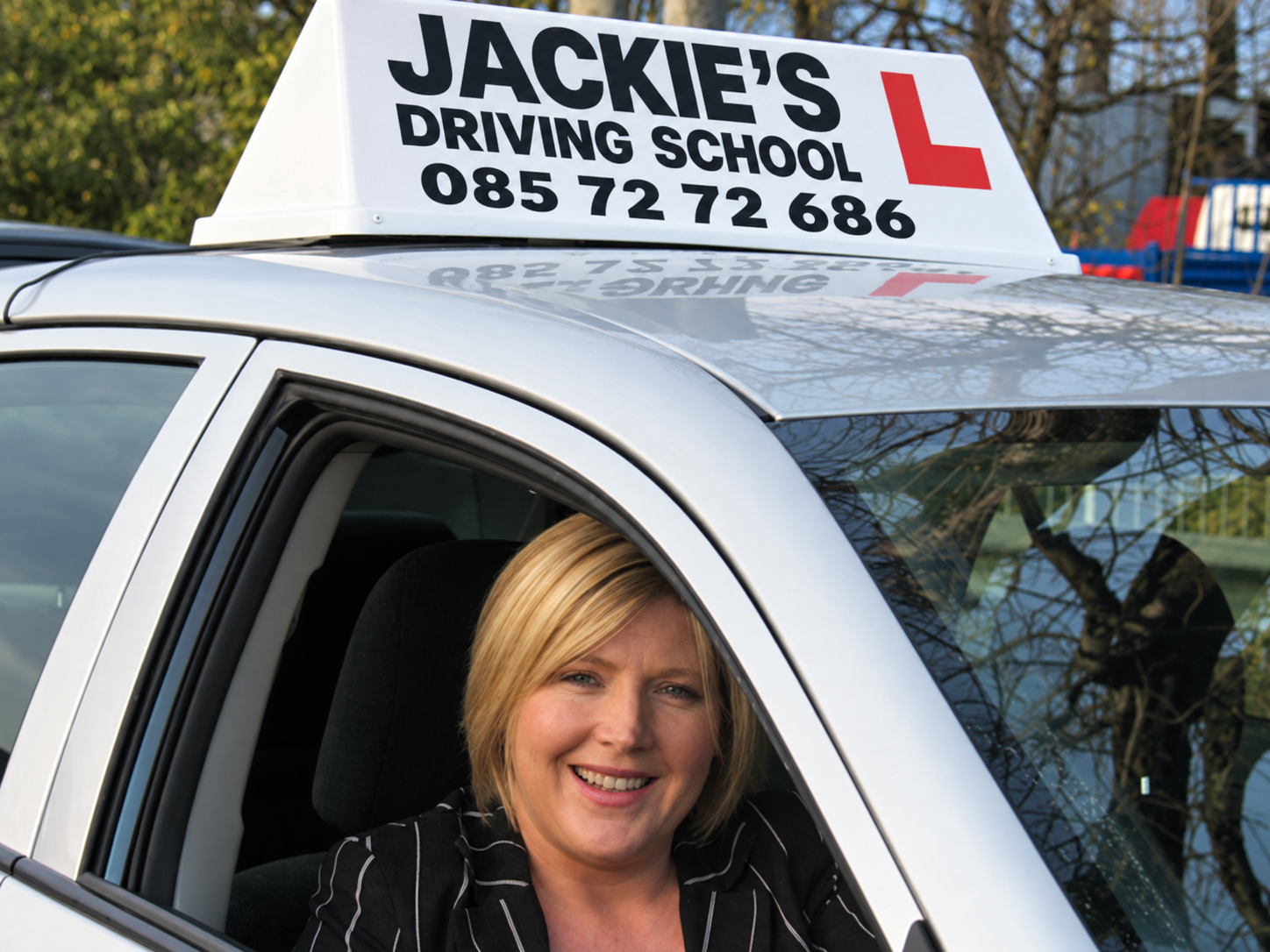 Close-up of Jacqueline Moran smiling from the driver's seat of a school car.